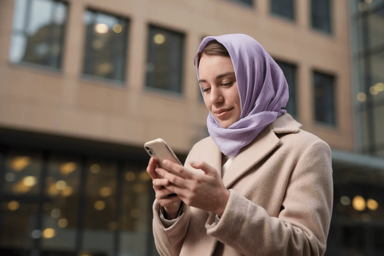 Young woman in a headscarf and coat using her smartphone, symbolizing engagement with digital tools for cognitive function and longevity.