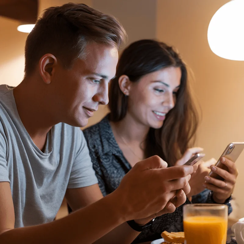 Couple smiling while looking at their smartphones, promoting general longevity through mindful tech use and connection.