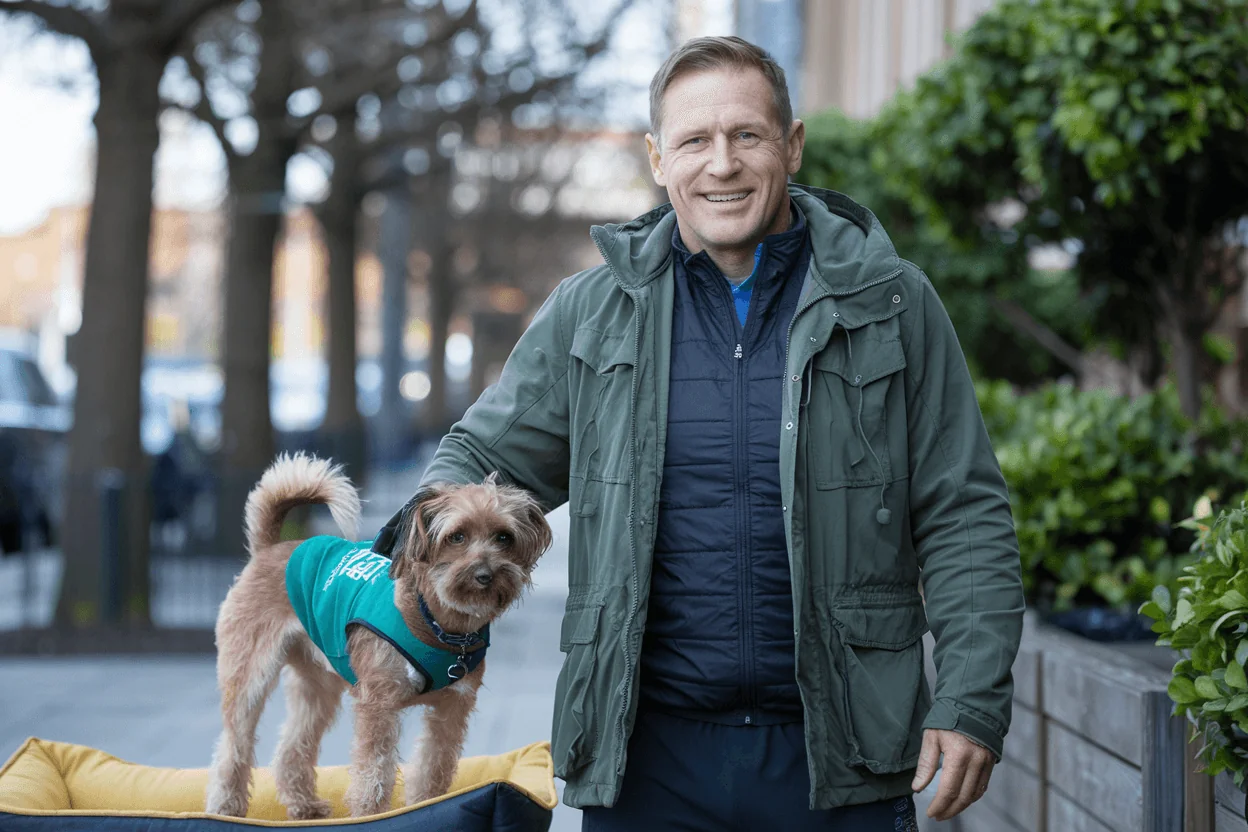 Smiling man with his dog in a turquoise vest, suggesting a healthy lifestyle and active life for glucose control and longevity.